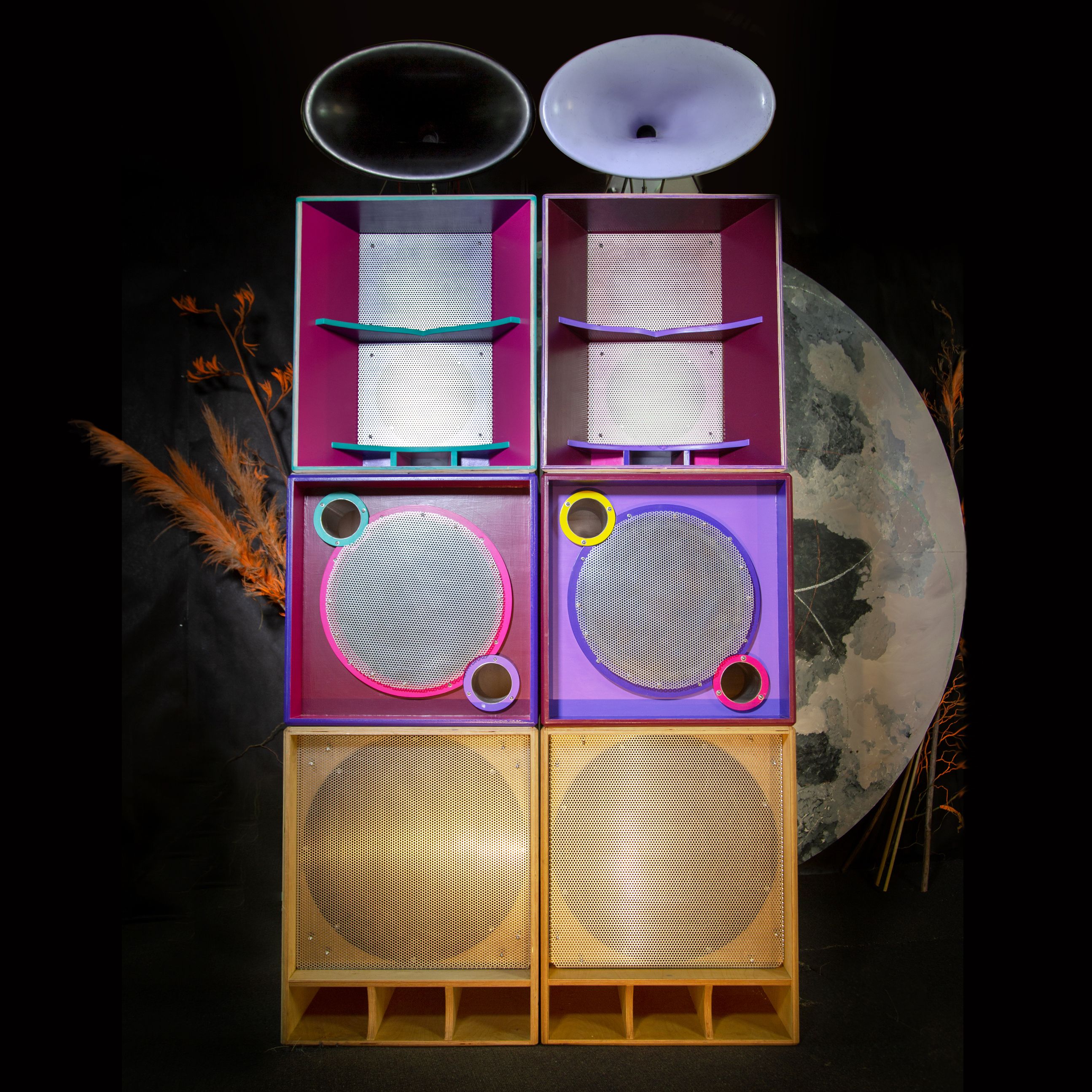 A colourful stack of speakers, in yellows, pinks and purples. A large moon peeks out from behind the stacks.